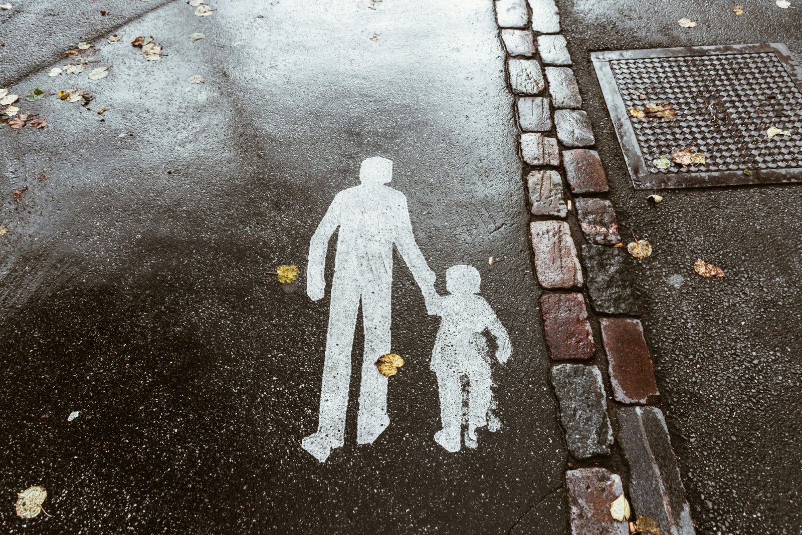 A pavement marking on wet asphalt showing an adult figure leading a child by the hand